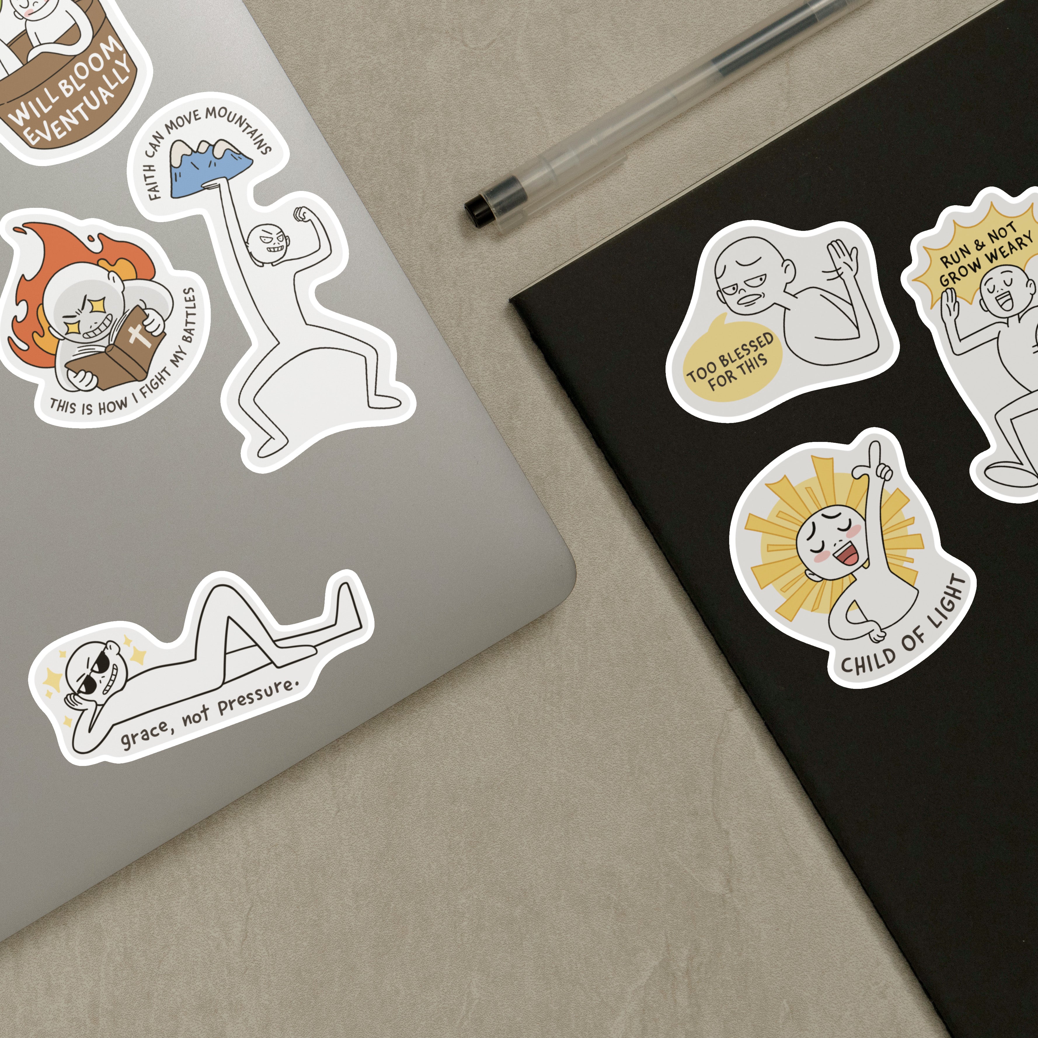 Laptop and notebook adorned with Everyday Believer stickers featuring Christian messages like "Grace, Not Pressure" and "Child of Light," from The Commandment Co, Singapore.