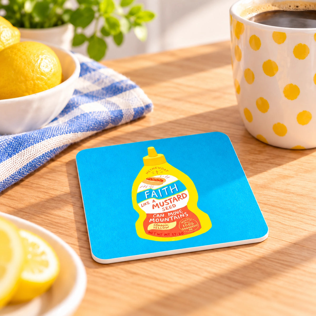 Faith Mustard Sauce Christian coaster lying flat on a sunlit table beside lemons and a mug.