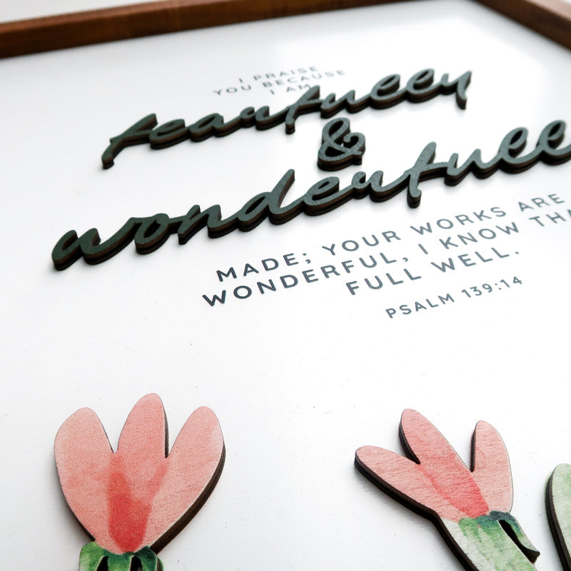Close-up view of a wooden scripture poster featuring the Bible verse Psalm 139:14, "Fearfully and wonderfully made," with layered 3D text and delicate floral accents.