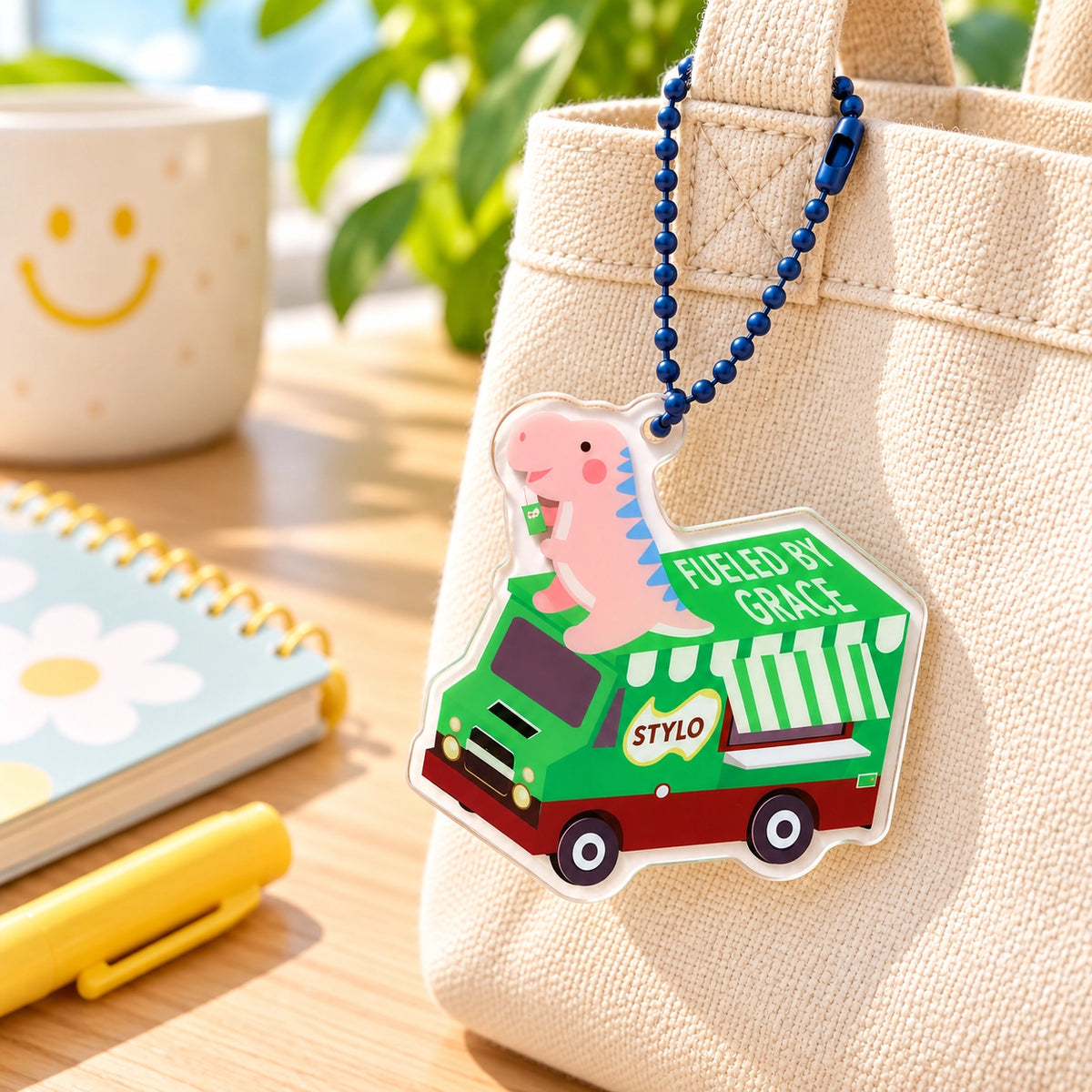 Fueled by Grace dinosaur malt beverage truck acrylic keychain hanging from a cream canvas tote bag.