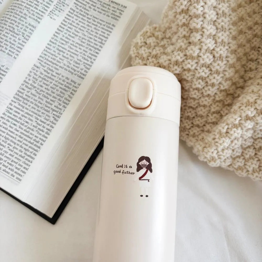 God Is a good Father Christian stainless steel thermal bottle beside an open Bible and knitted blanket