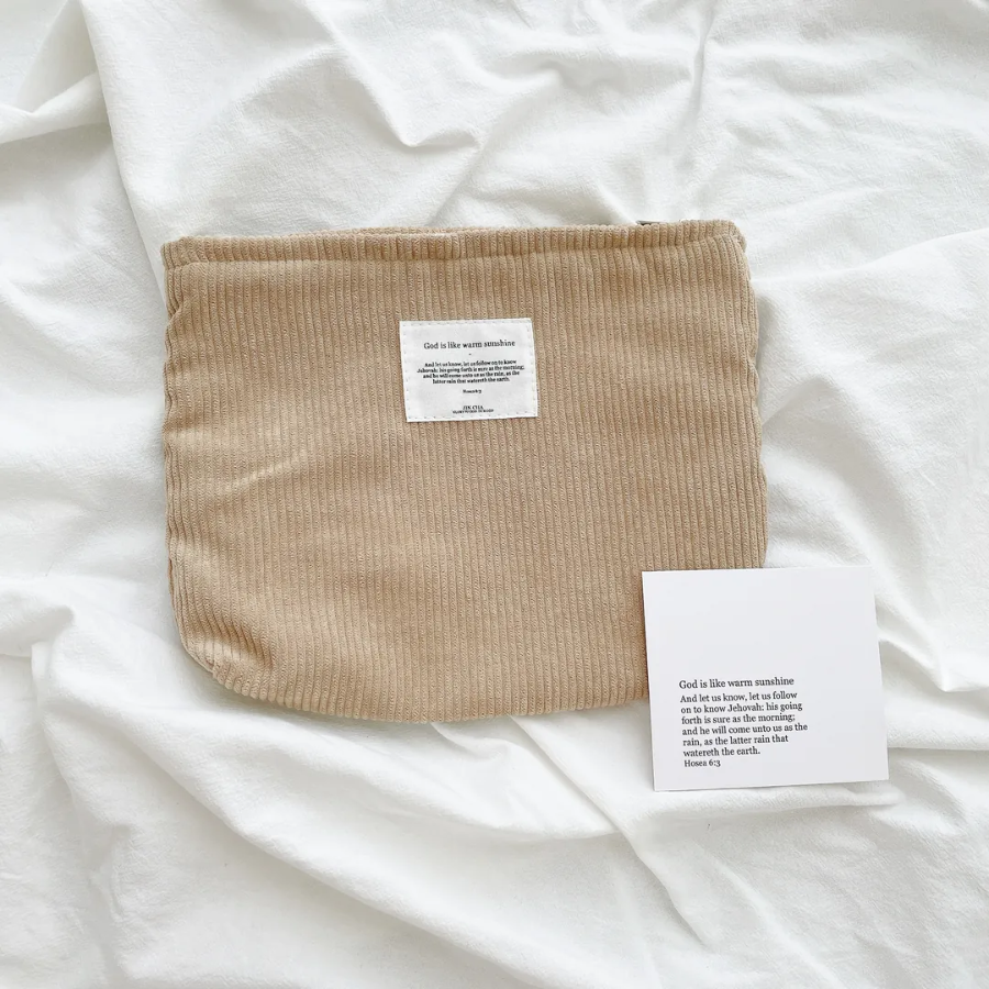 God is like warm sunshine beige corduroy zipper clutch with an inspirational message patch, placed on a textured white fabric, radiating simple happiness and encouragement.
