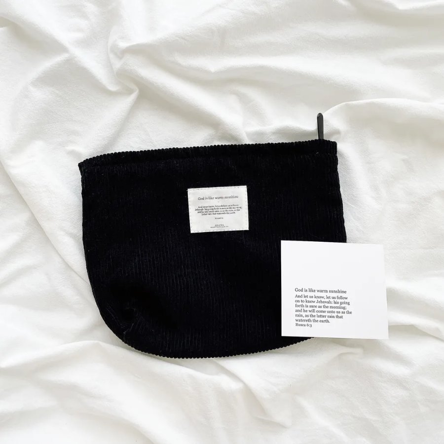 God is like warm sunshine black corduroy zipper clutch with an inspirational message patch, displayed on a soft white fabric alongside an encouragement card, reflecting simple happiness and faith.
