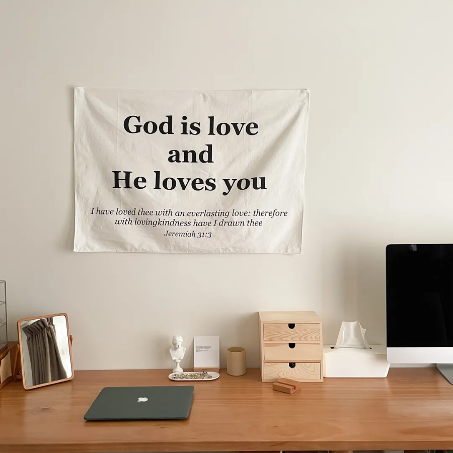 Minimalist wall tapestry with the message "God is love and He loves you" and Jeremiah 31:3 Bible verse, displayed above a wooden cabinet with decorative items, inspiring faith, comfort, and simple happiness.