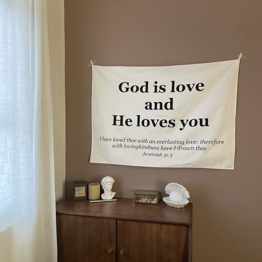 Minimalist wall tapestry with the message "God is love and He loves you" and Jeremiah 31:3 Bible verse, hanging above a tidy wooden desk, inspiring faith, encouragement, and simple happiness.