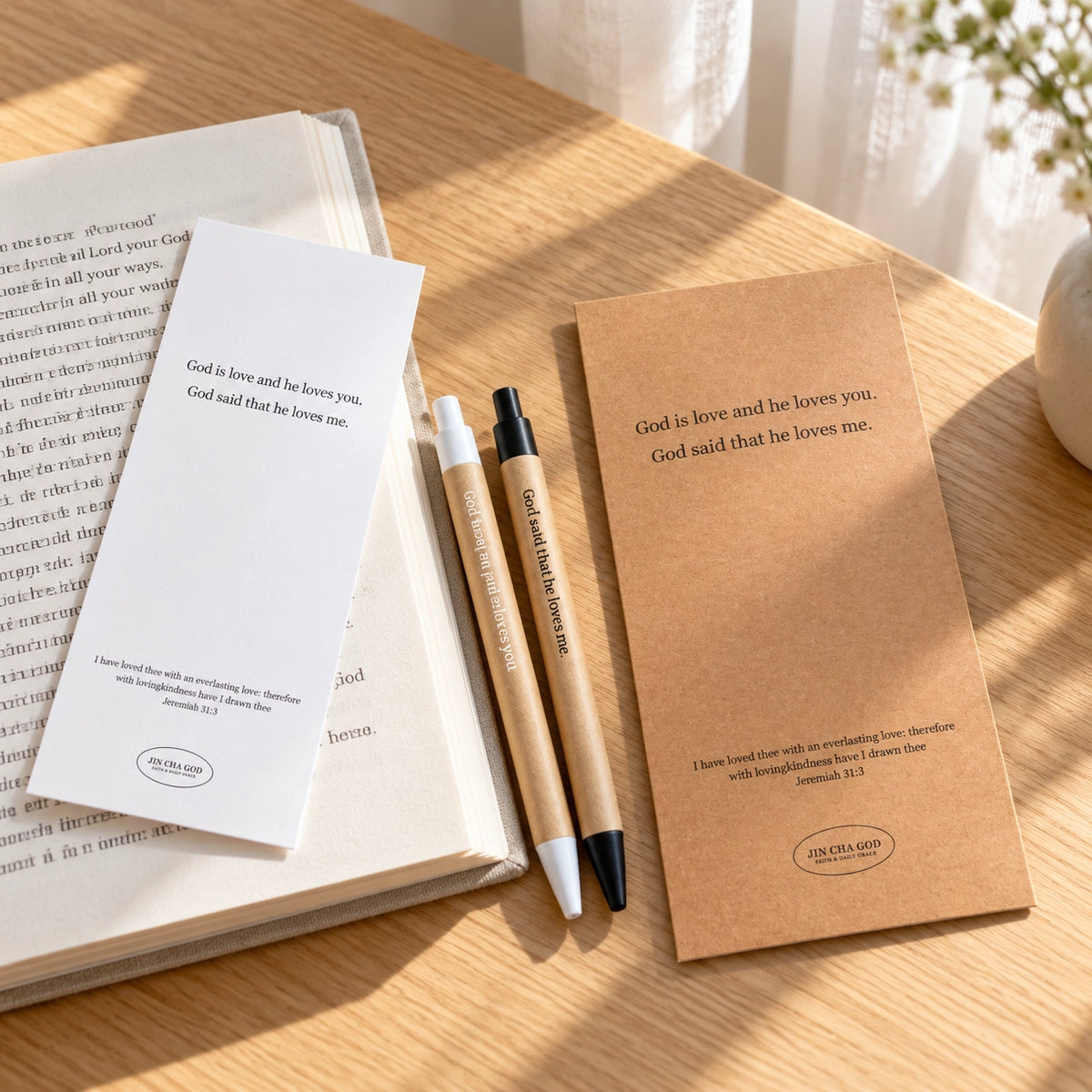 God is Love pens and bookmark set styled on a warm wooden table beside an open book