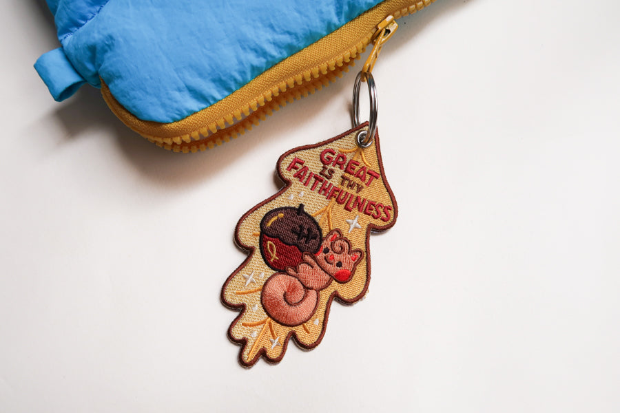 Embroidered Christian keychain with “Great Is Thy Faithfulness” text featuring cozy woodland animals on warm leaf-shaped background.
