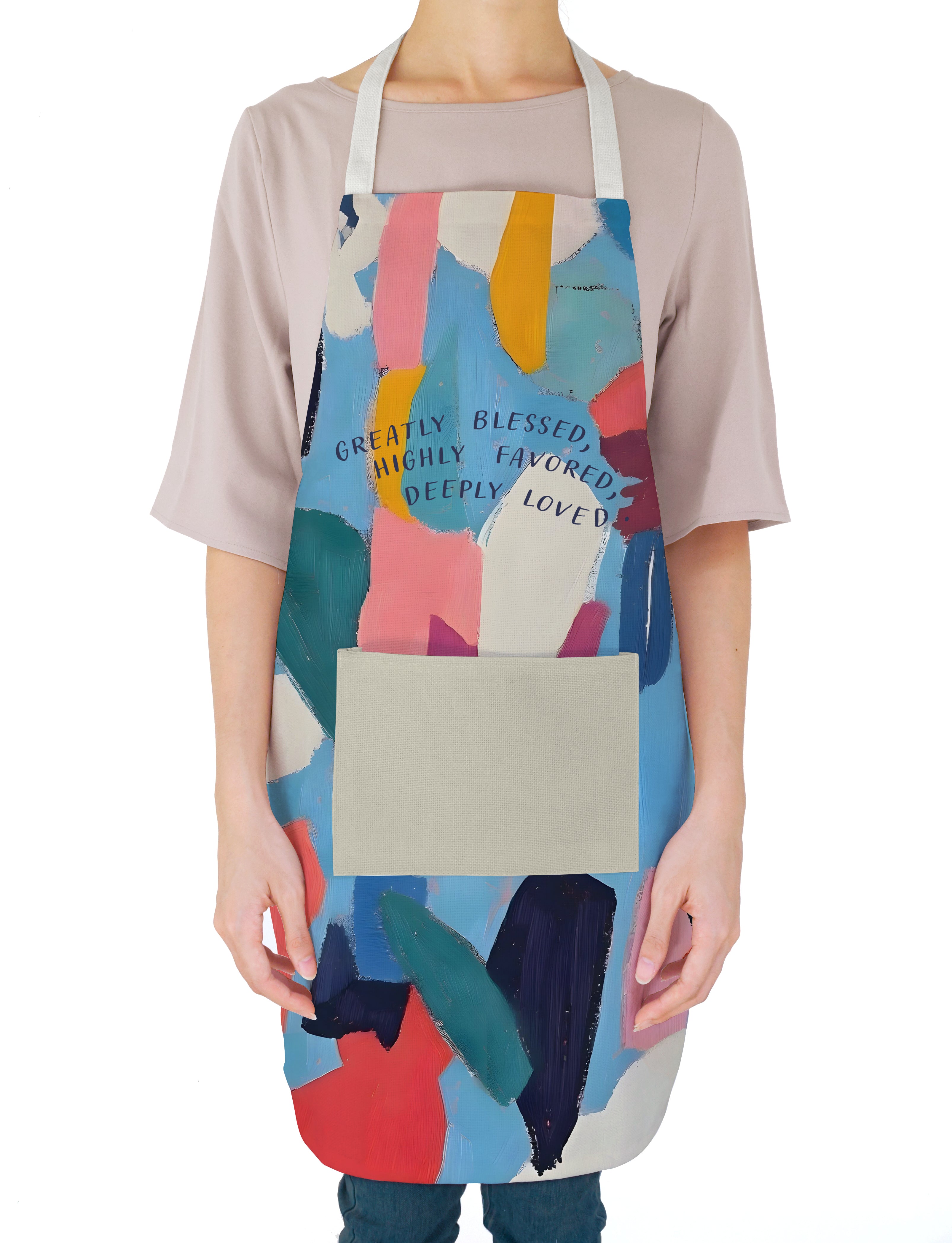 person wearing a colorful "Greatly Blessed, Highly Favored, Deeply Loved" apron with abstract brushstroke patterns, inspiring faith, encouragement, and simple happiness in everyday life.