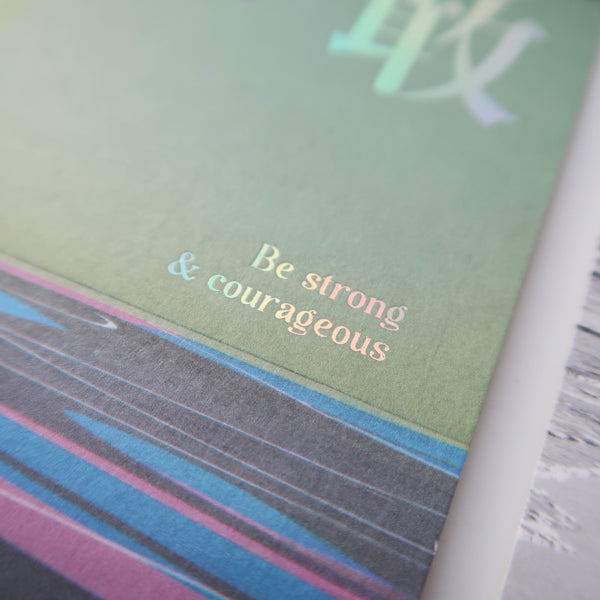 A detailed view of a postcard with the motivational text "Be strong & courageous," printed on a colorful background with soft pastel tones.