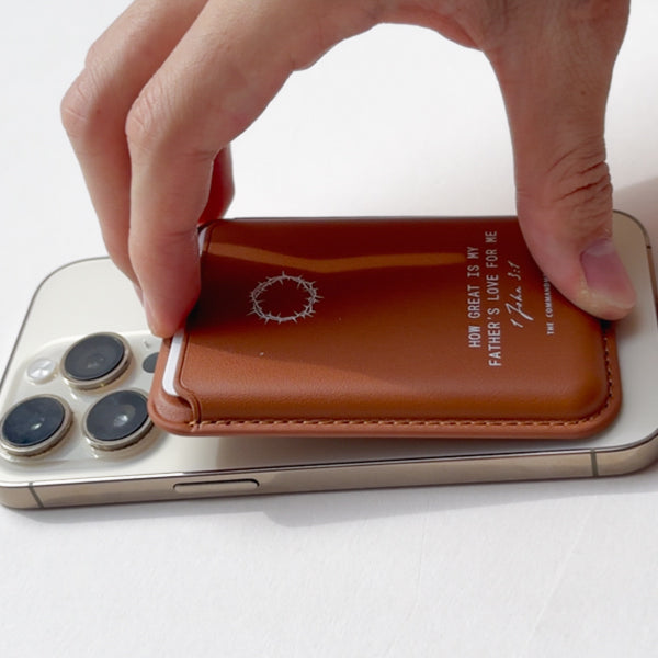 A hand attaching a Brown Leather Magsafe Wallet to the back of a mobile phone