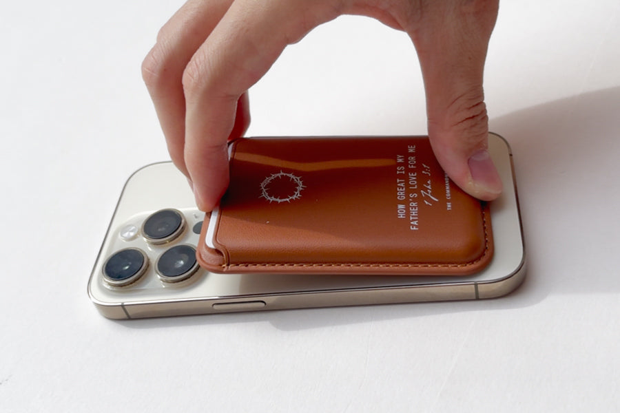 A hand attaching a Brown Leather Magsafe Wallet to the back of a mobile phone