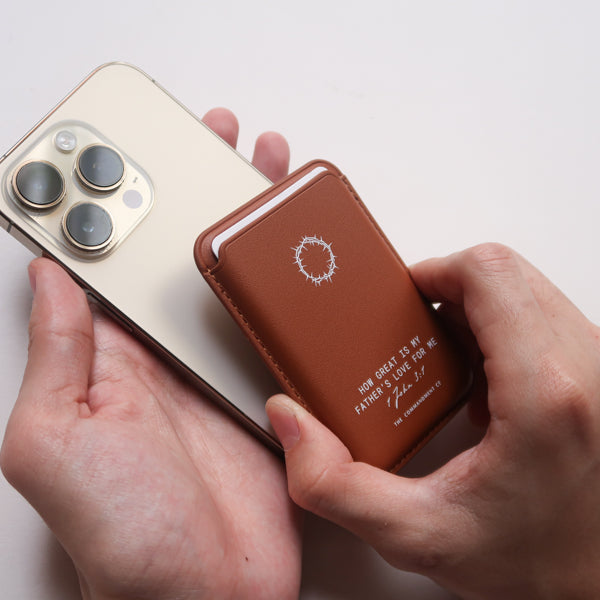 A pair of hands attaching a Brown Leather Magsafe Wallet to the back of a mobile phone