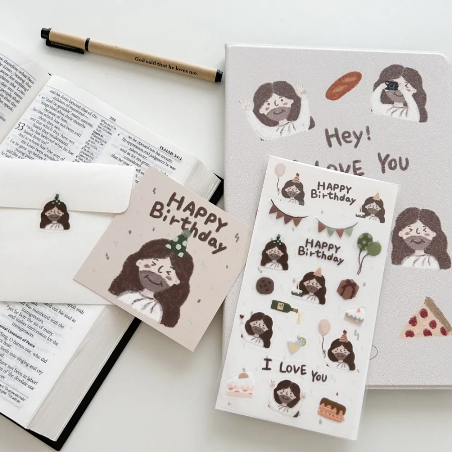 "Happy Birthday" sticker sheet and postcard with cute Jesus illustrations, matching envelope, and Christian stationery, arranged with an open Bible and pen, spreading encouragement and simple happiness.