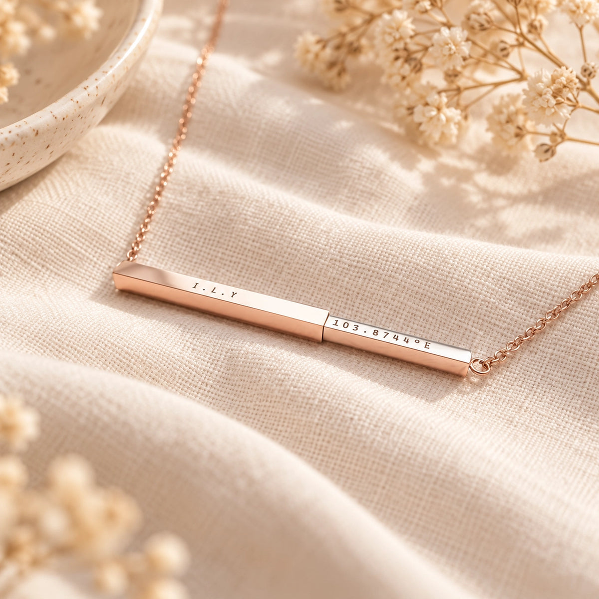 Rose gold personalised hidden message bar pendant necklace styled on soft cream linen with dried flowers
