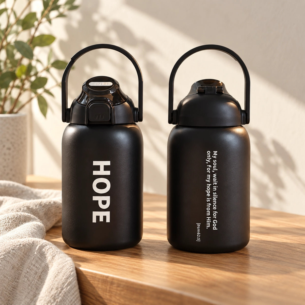 Hope black travel tumbler shown front and back on a sunlit wooden surface.