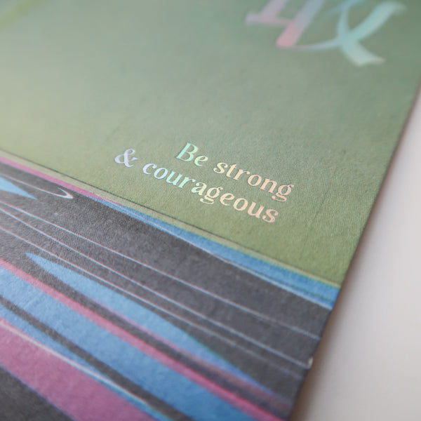 A detailed view of a postcard with the motivational text "Be strong & courageous," printed on a colorful background with soft pastel tones.