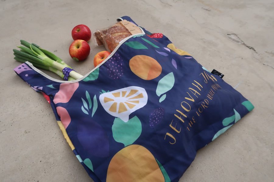 Close-up of foldable
reusable shopping bag with
Bible verse "Jehovah Jireh"
and fruit design, filled with
groceries, perfect for
Christian gifts and Christian
gift stores.