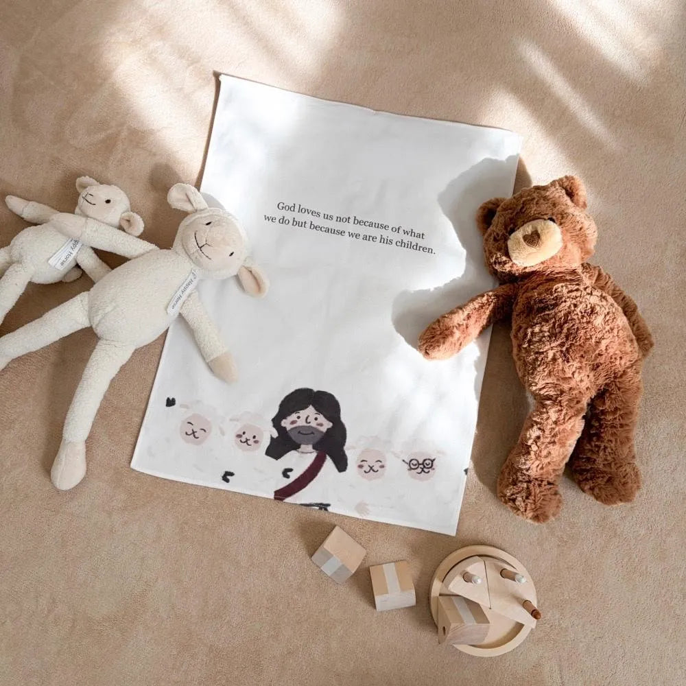 Christian cotton linen wall decor with text "God loves us not because of what we do but because we are his children", styled with sheep and bear plush toys in a warm neutral room