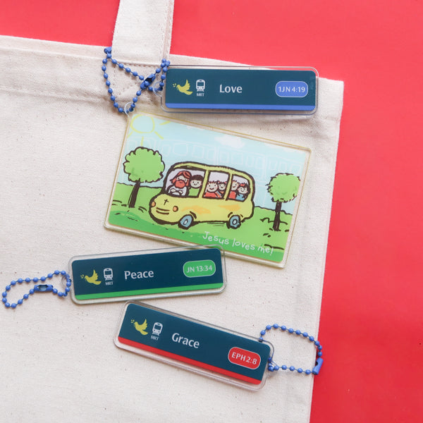 Singapore-inspired Christian acrylic keychains on a tote bag featuring Jesus Loves Me transport card, Love, Peace, and Grace MRT sign designs