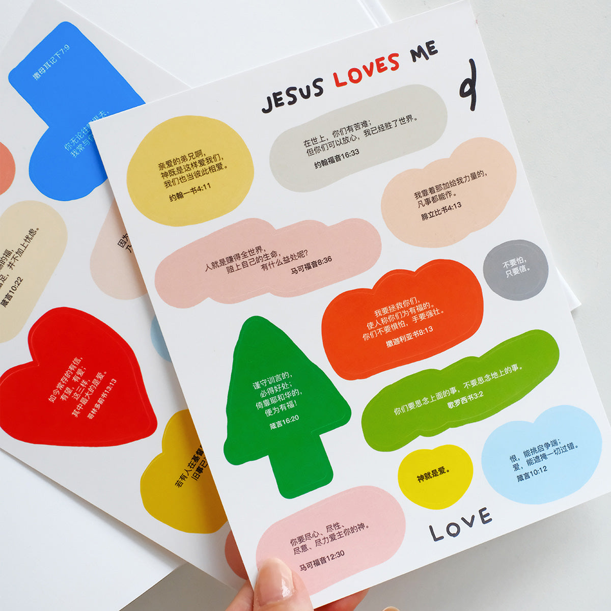 Colorful sticker sheet titled 'Jesus Loves Me' with various Bible verse quotes and Christian inspirational messages in playful shapes.