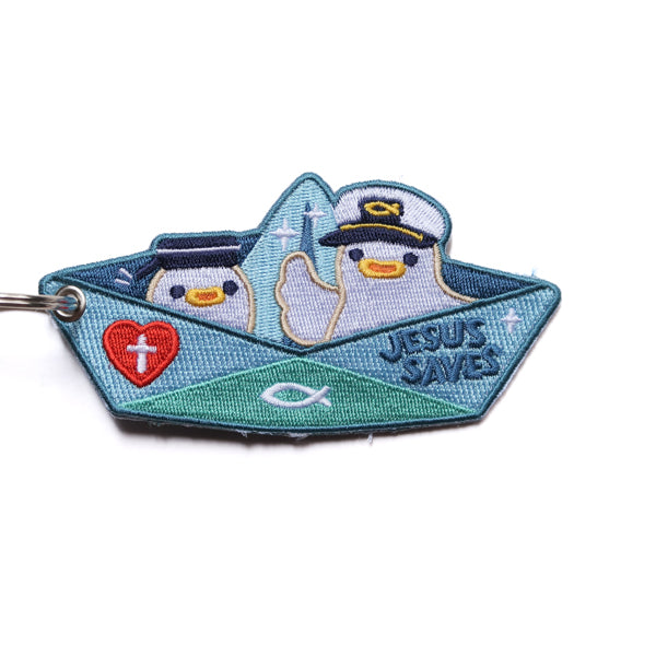 Embroidered Christian paper boat keychain with “Jesus Saves” text, red cross heart and fish symbol on blue background.