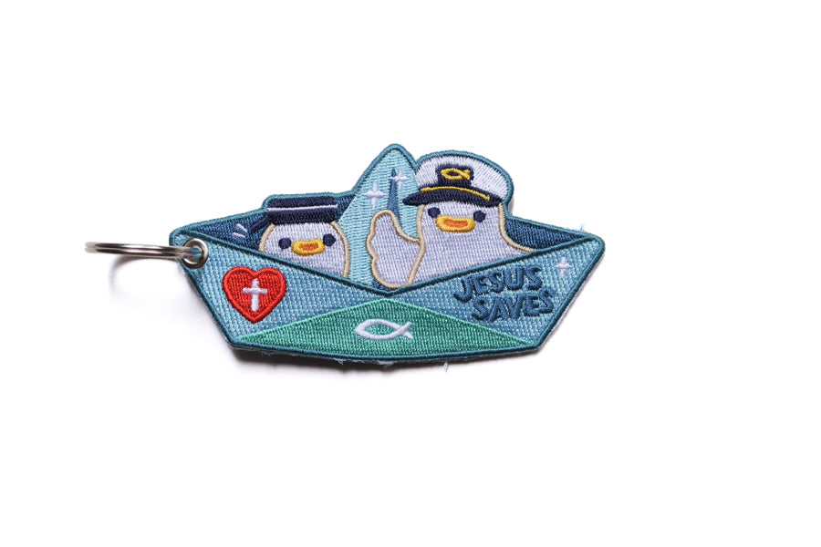 Embroidered Christian paper boat keychain with “Jesus Saves” text, red cross heart and fish symbol on blue background.