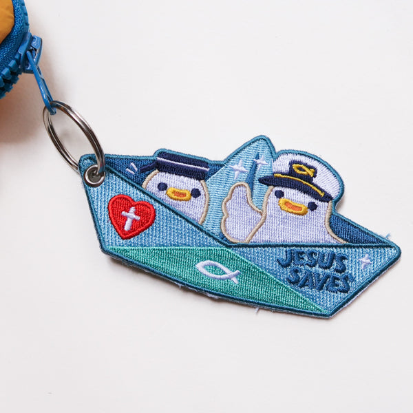 Jesus Saves embroidered Christian keychain featuring cute sailor characters in a paper boat design clipped onto zipper.
