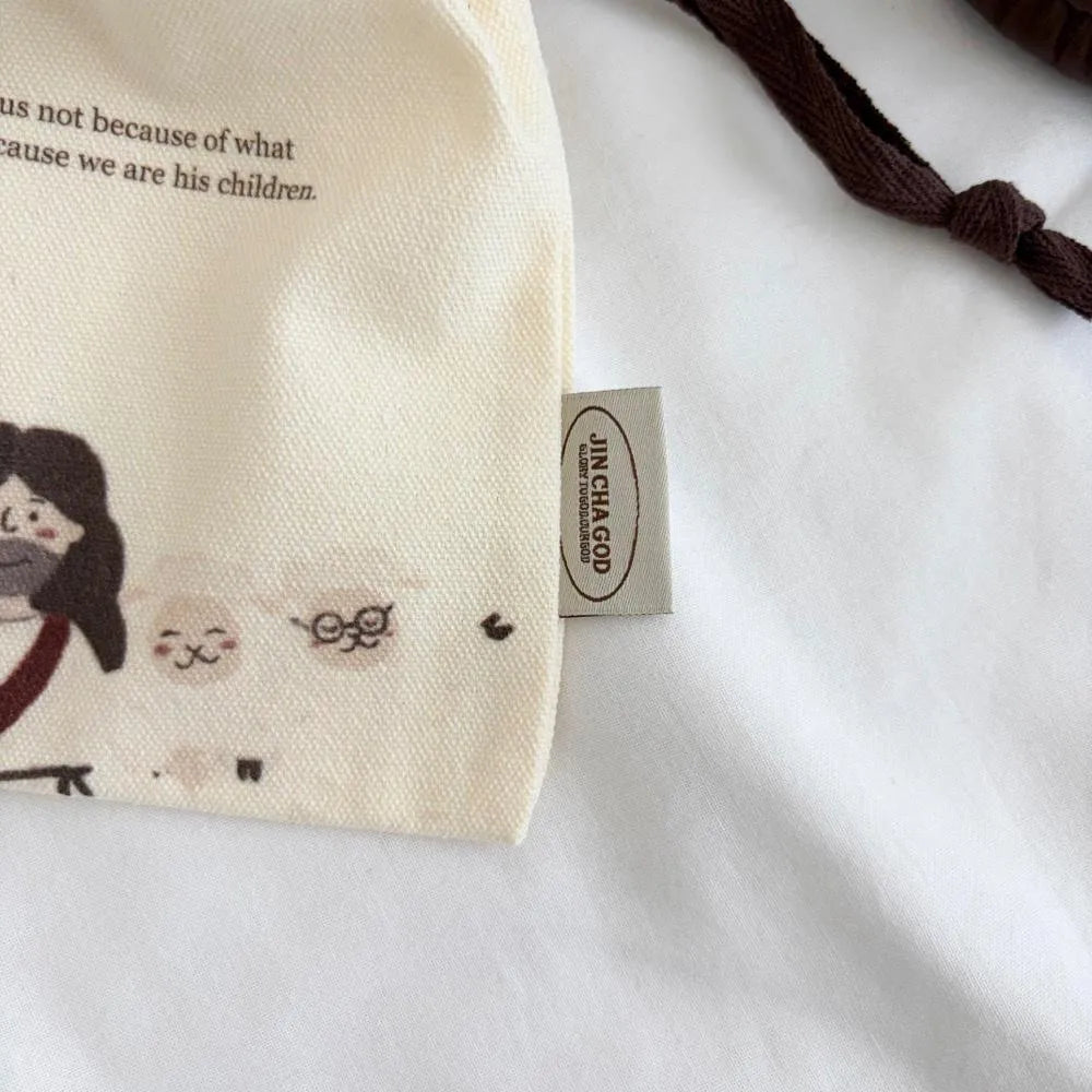 Close-up of a Christian canvas drawstring pouch featuring a Jesus and sheep illustration with textured fabric and woven brand label