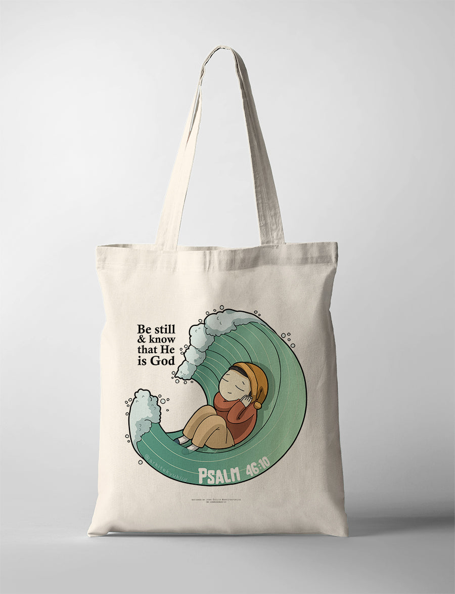 Christian tote bag collaboration between John Euclid and The Commandment Co featuring illustrated character resting inside an ocean wave with the phrase “Be still and know that He is God” from Psalm 46:10