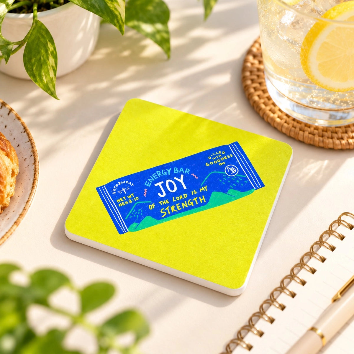 Joy Energy Bar Christian coaster featuring Nehemiah 8:10 styled on a bright sunlit desk with a lemon drink and notebook.