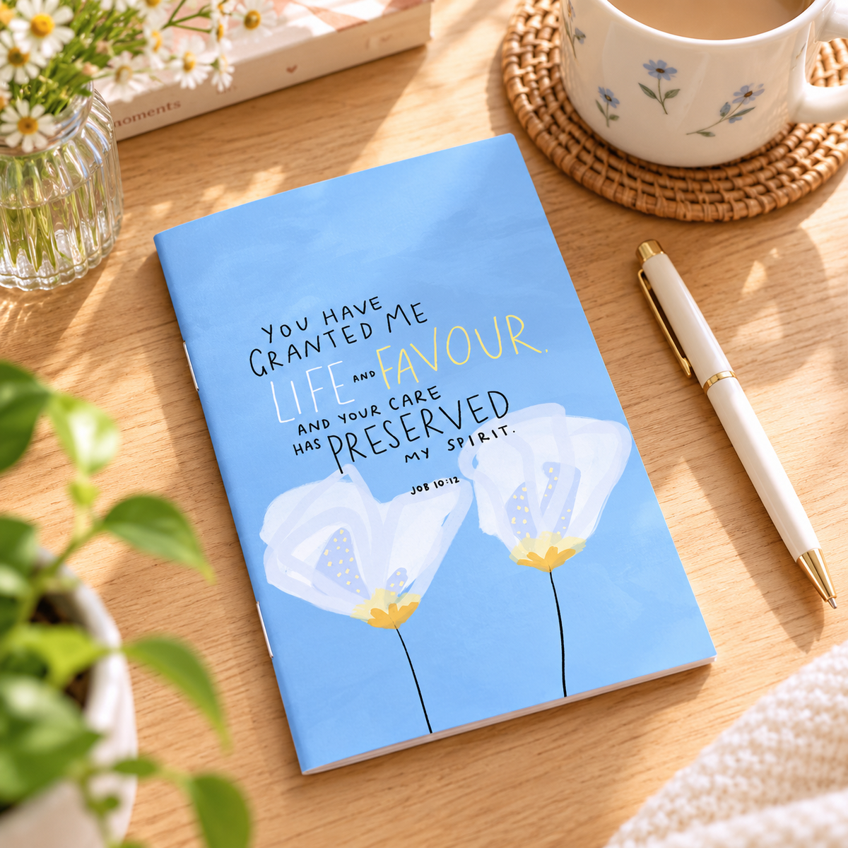 Life & Favour A6 Christian notebook inspired by Job 10:12 styled on a warm wooden desk with flowers, coffee and a pen