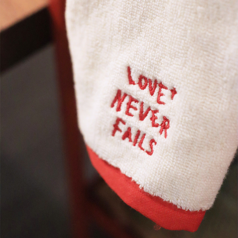 Love Never Fails embroidered cotton towel product view.