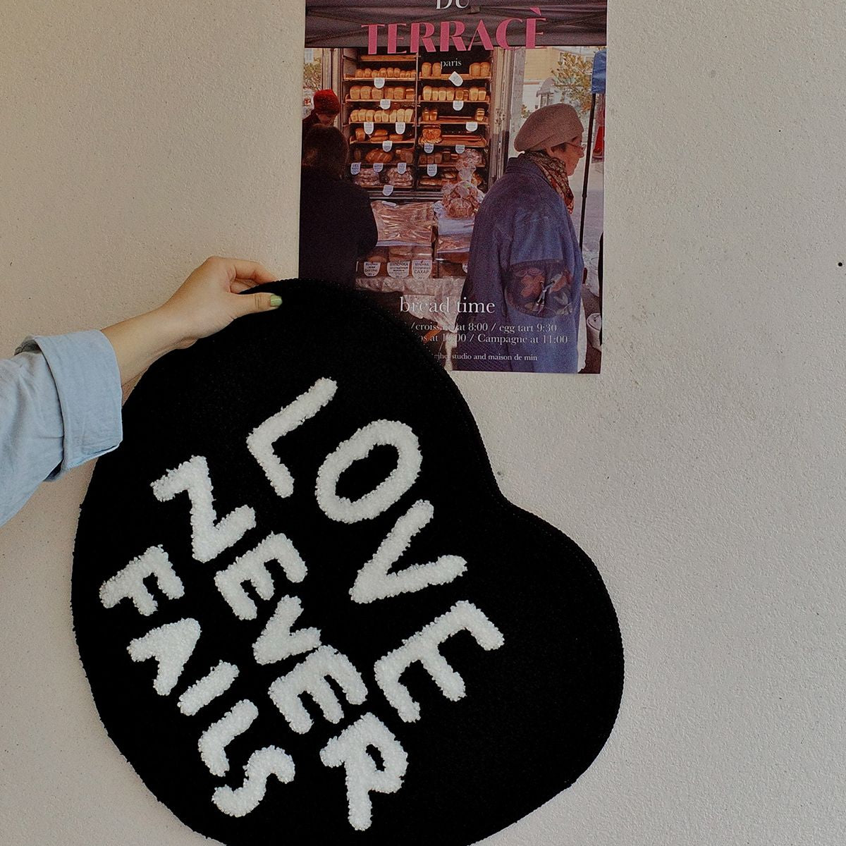 Lifestyle photo of a Love Never Fails heart-shaped tufted rug held against a wall, suitable as a Christian gift.