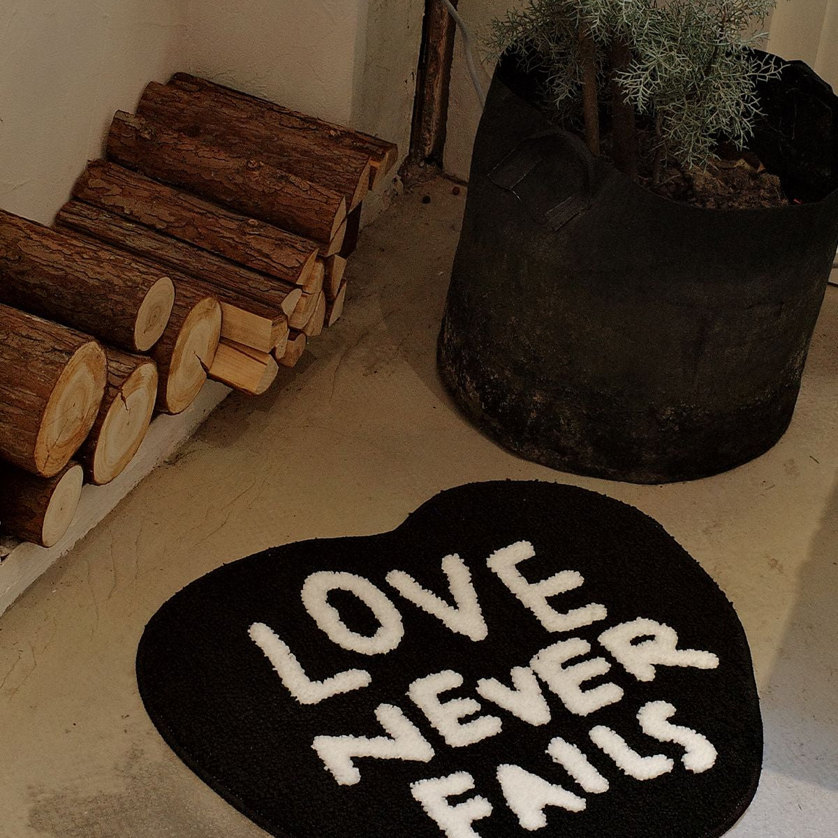 Top-down view of the Love Never Fails heart-shaped rug showing white tufted text on a black background.