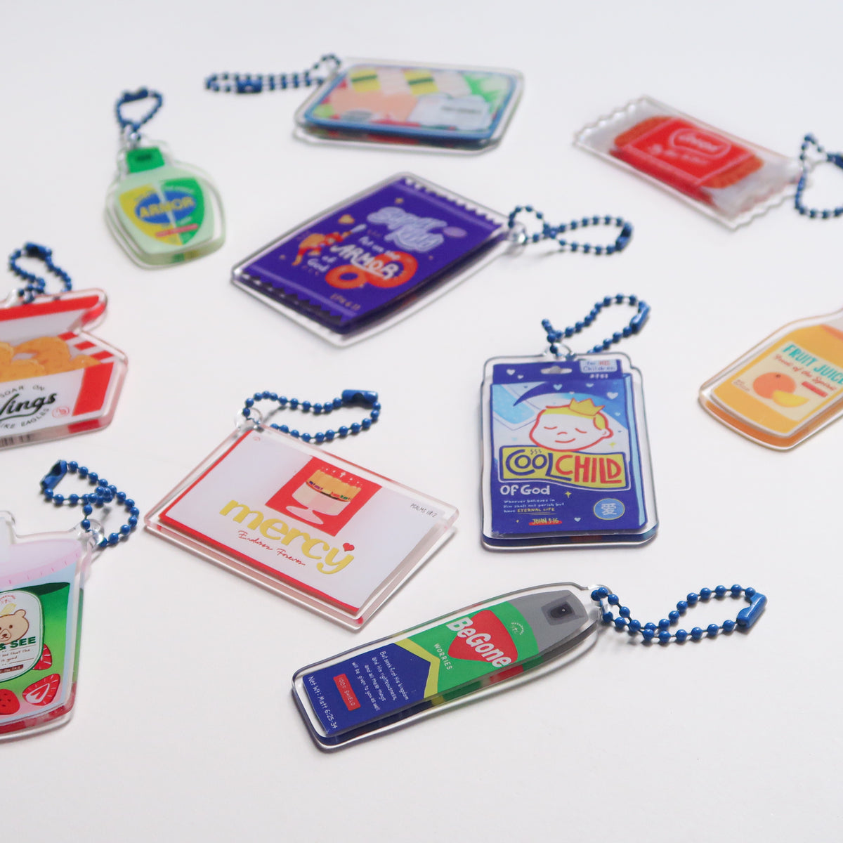 Flat lay of Love Supermarket acrylic keychain collection, including designs like sushi set, Cool Child patch, Armor of God, Begone Worries spray, fried wings, and more.