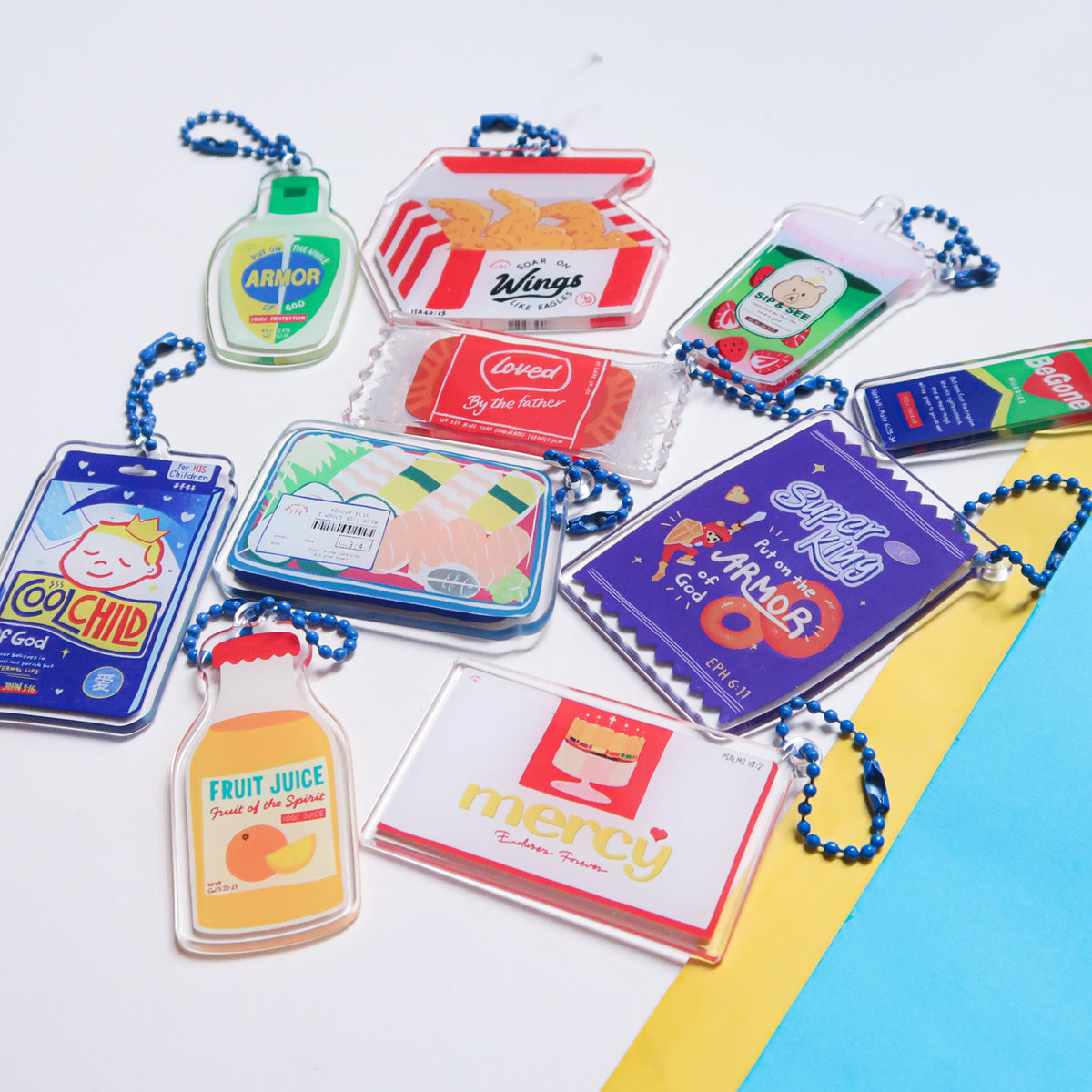 Complete Love Supermarket acrylic keychain collection displayed on a blue and yellow background, featuring ten playful faith-based designs.