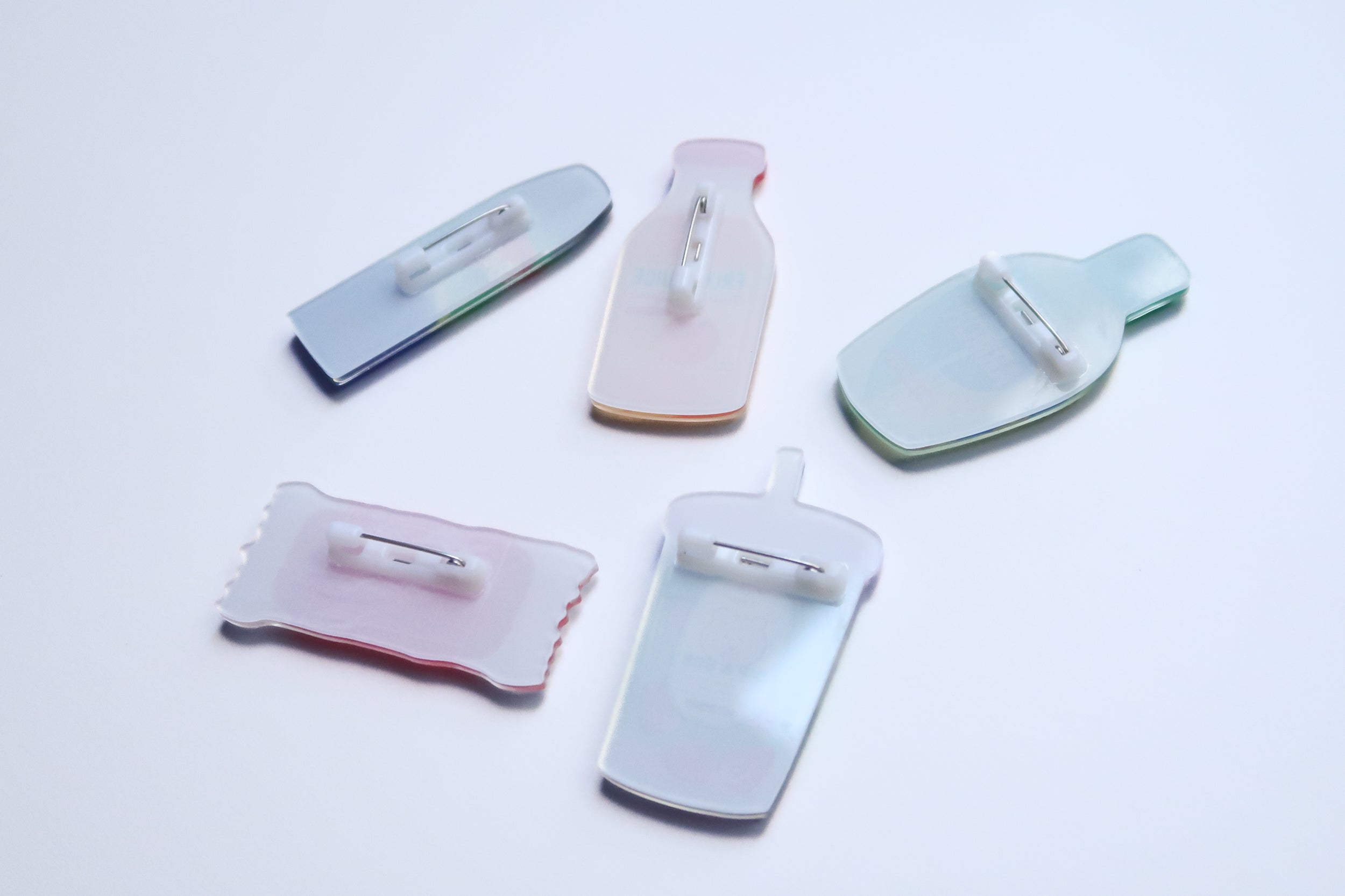 Back view of Love Supermarket acrylic pins showing pin fastenings and pastel acrylic backing for multiple snack-shaped Christian designs.