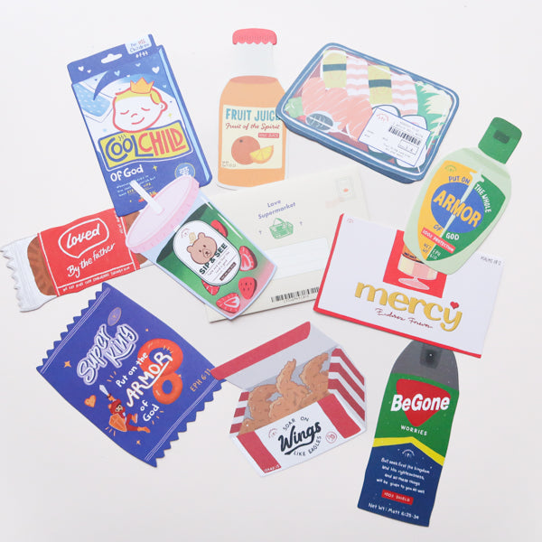 Flatlay of the Love Supermarket card set featuring 10 uniquely shaped Christian postcards inspired by food and household items.