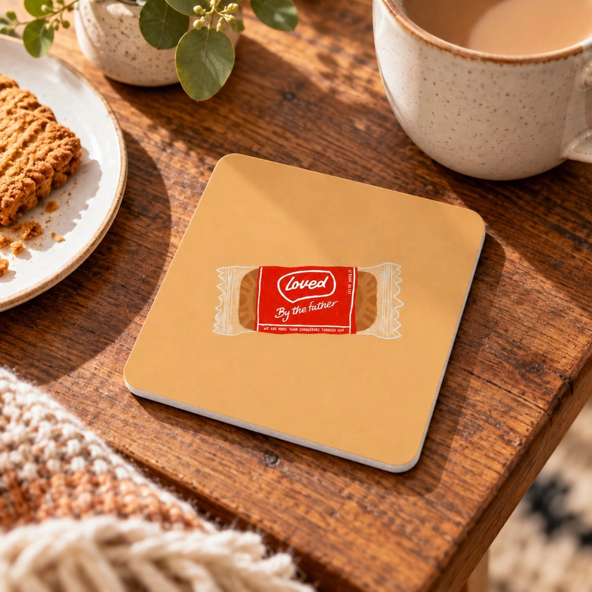Loved by the Father coffee biscuit Christian coaster from the LOVE SUPERMARKET collection on a warm wooden table.