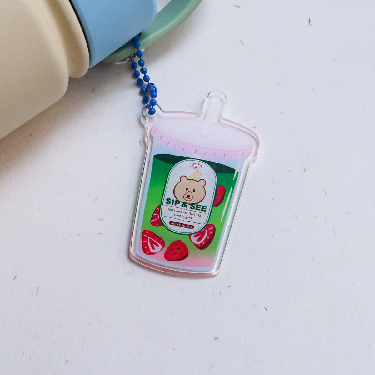 Sip & See strawberry matcha drink acrylic keychain attached to a water bottle, featuring a cute bear illustration and the verse “Taste and see that the Lord is good.”