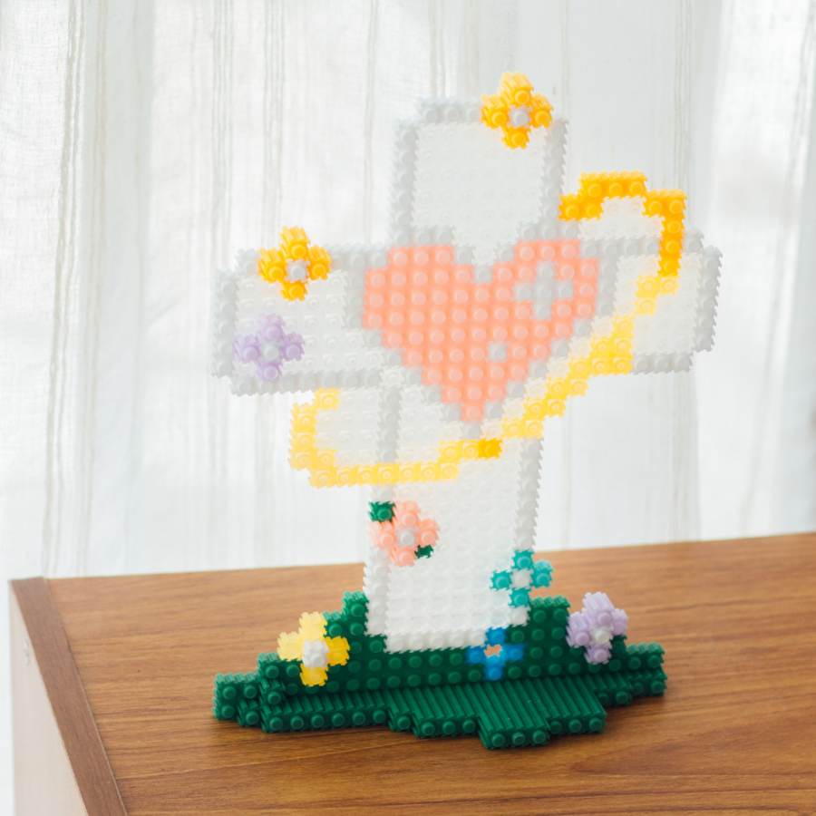Micro building set cross with a heart and floral decorations, symbolizing hope and light, displayed on a wooden table to inspire simple happiness and encouragement.