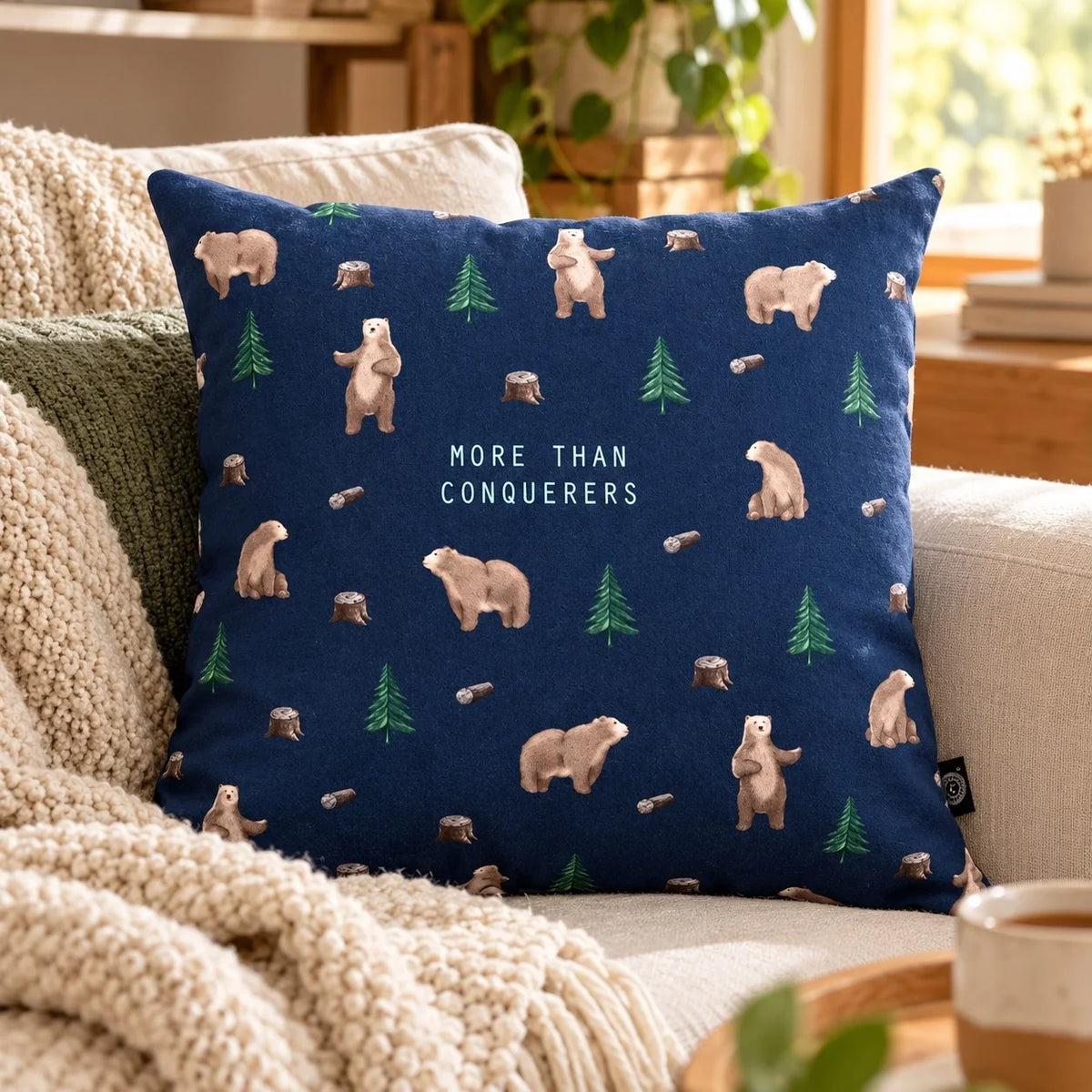 More Than Conquerors navy blue cushion cover with bears and trees on a sofa.