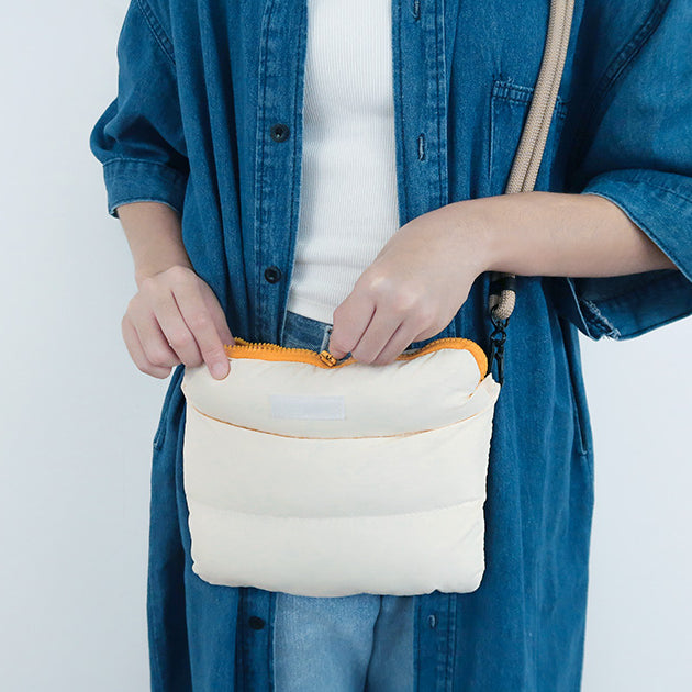 Person opening the oat-colored multi-purpose bag, showing its durable zipper and padded texture.