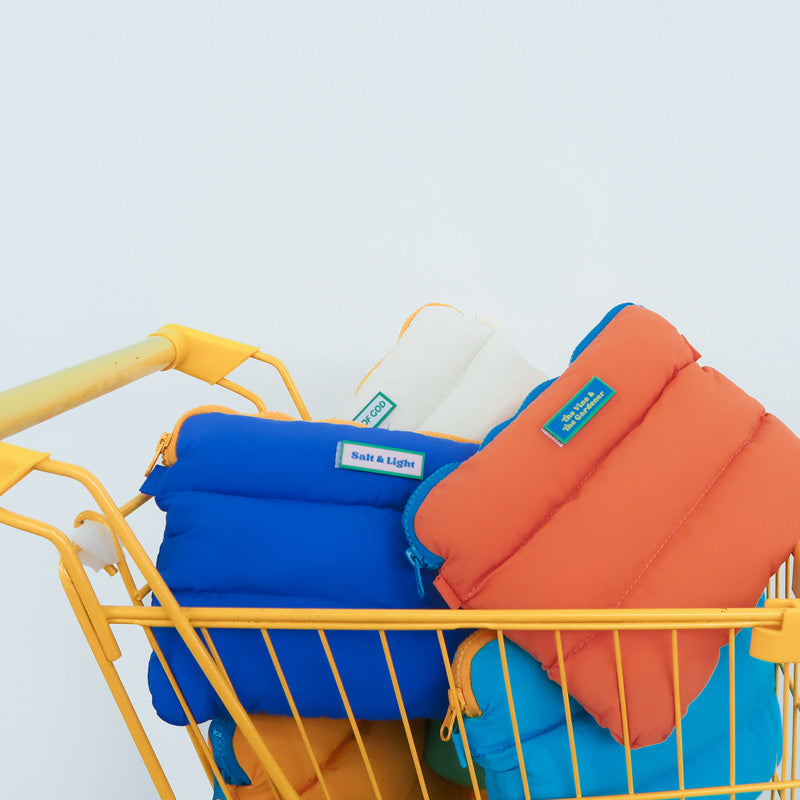 Colorful Pong Pong Bags displayed in a vibrant yellow shopping cart, featuring blue, orange, and white designs with unique velcro patches that read 'Salt & Light' and 'The Vine & The Gardener.'