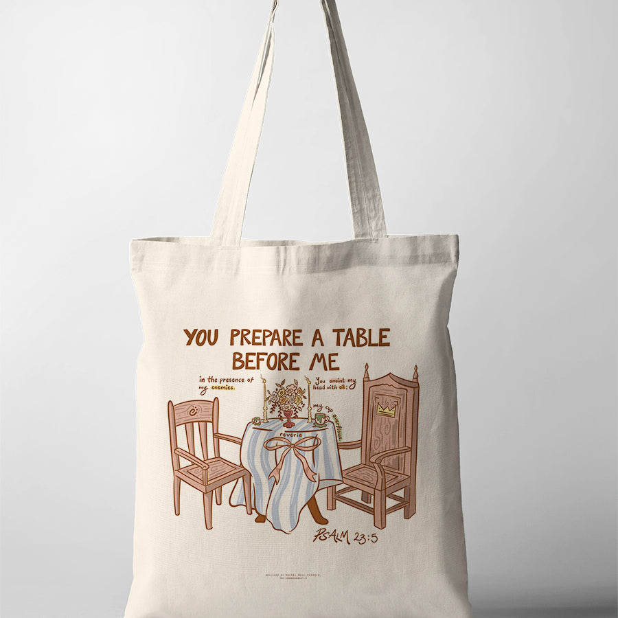 Canvas Christian tote bag featuring Psalm 23:5 illustration of a table with chairs and the phrase “You prepare a table before me” in a warm minimal design