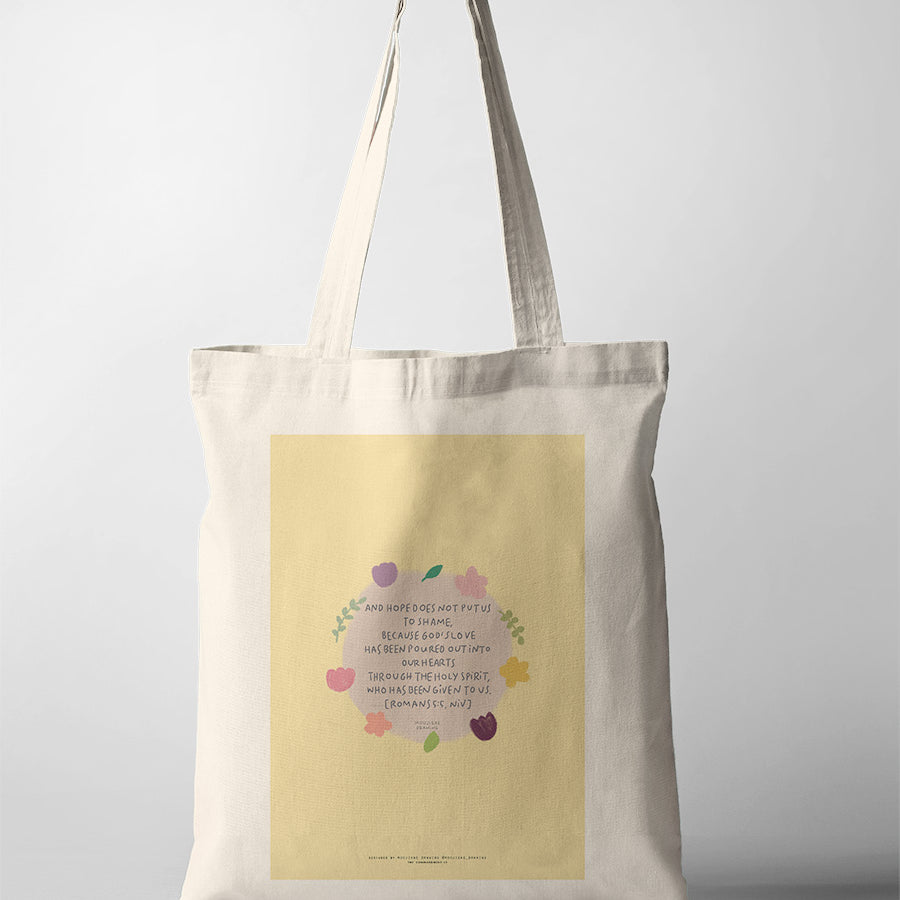 Christian tote bag featuring Romans 5:5 with floral artwork about God’s love poured into our hearts