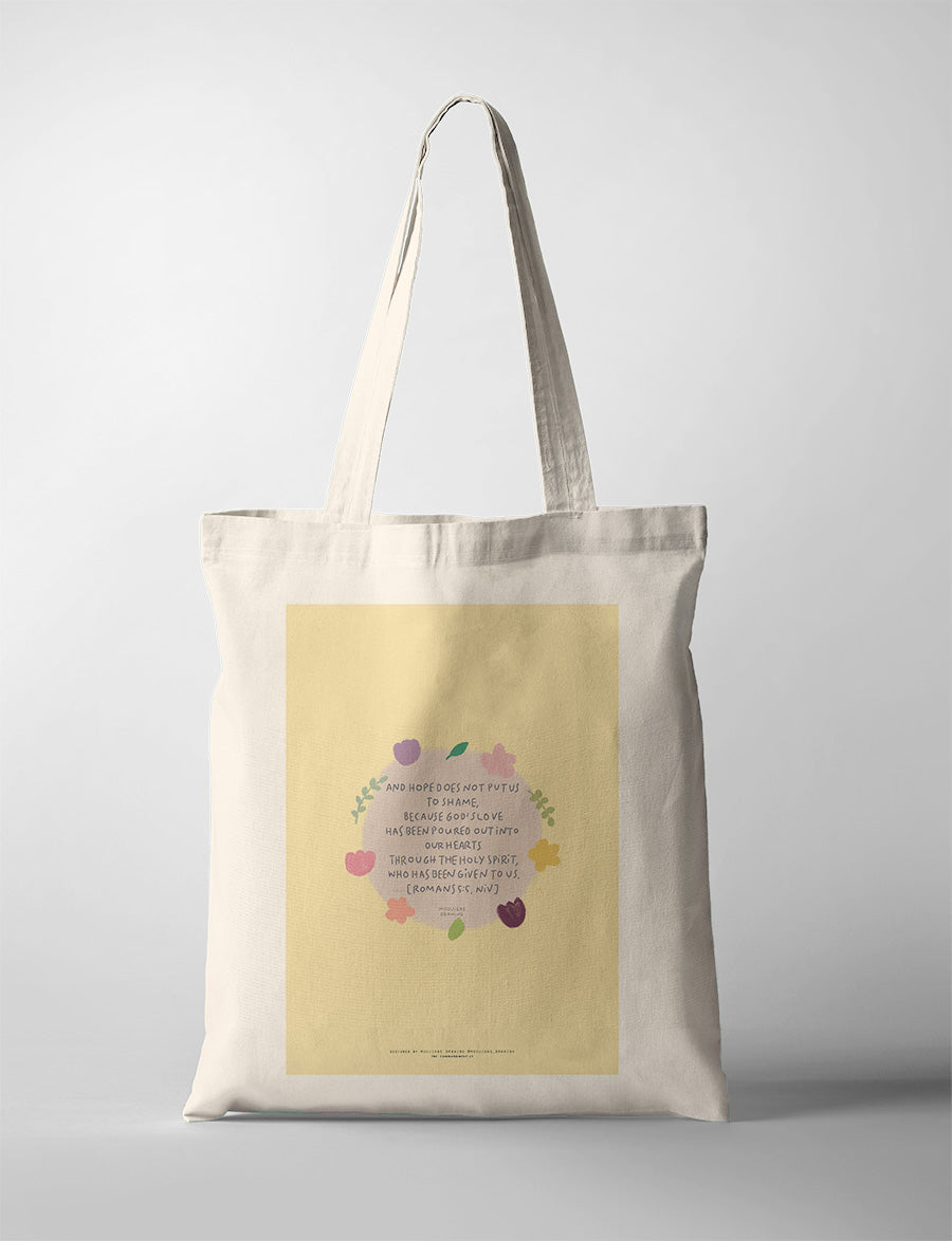 Christian tote bag featuring Romans 5:5 with floral artwork about God’s love poured into our hearts