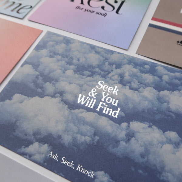 A close-up view of a collection of inspirational postcards, featuring the "Seek & You Will Find" card with a sky and clouds background, alongside other cards with uplifting messages.