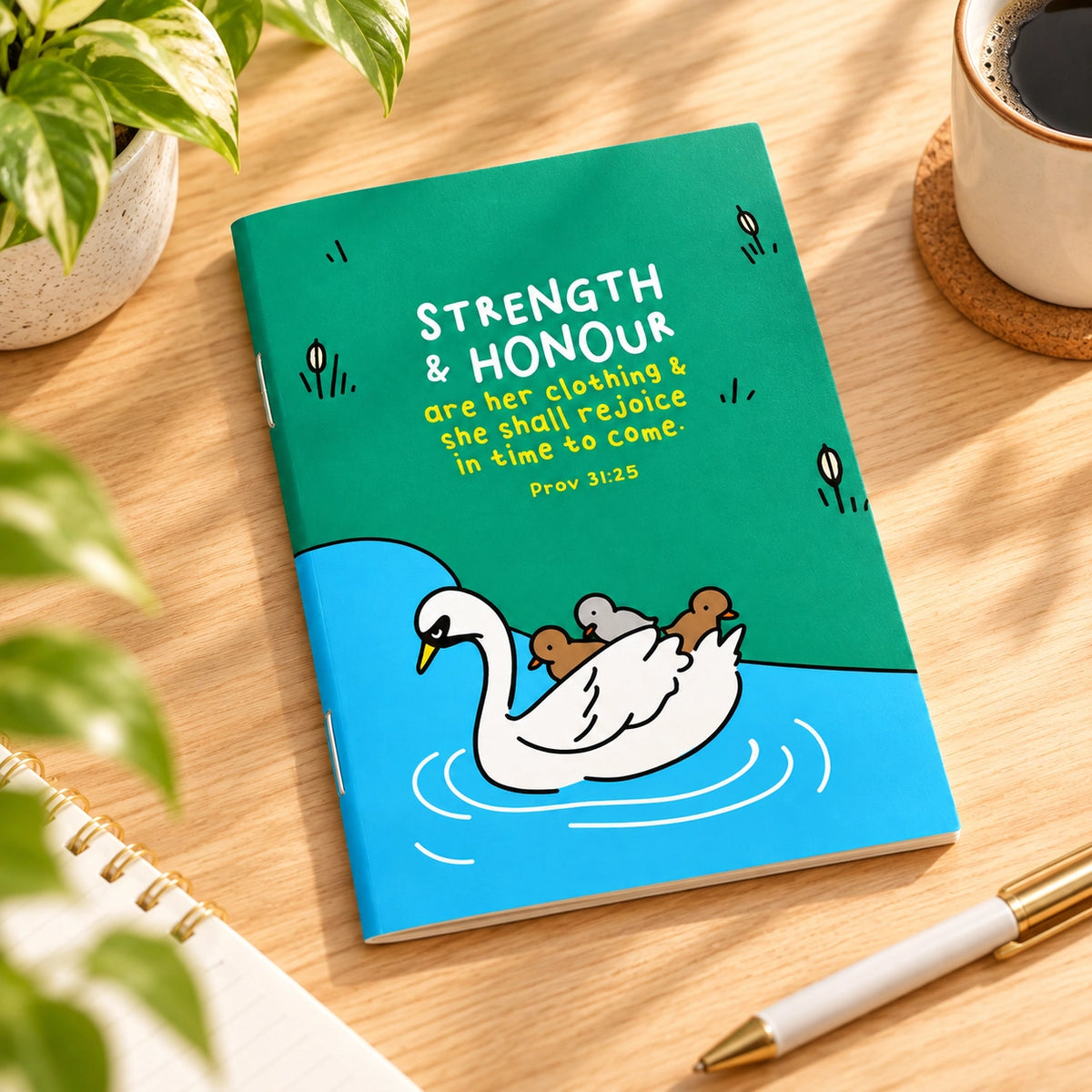 Strength and Honour A6 Christian notebook lying on a bright wooden desk with coffee, pen and greenery