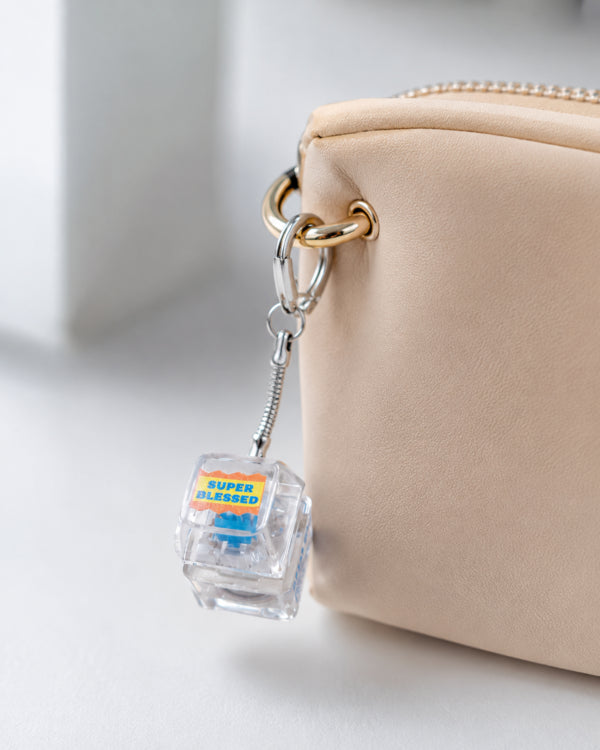 Super Blessed light-up keycap keychain clipped to a beige bag